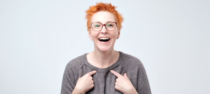 Woman pointing at herself with both hands, looking happy and surprised